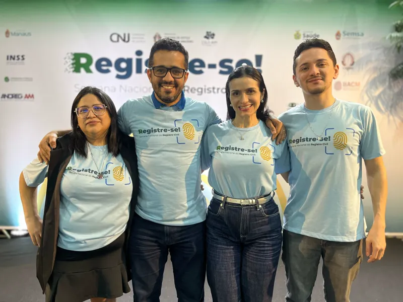 Equipe do Cartório Manauara, com camisetas do Registre-se!, diante do painel da Semana Nacional do Registro Civil.