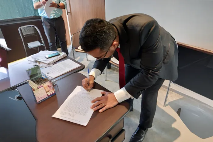 O Registrador Civil Titular Miguel Jaime dos Santos Agra assina documento sobre uma mesa durante a transmissão do acervo.